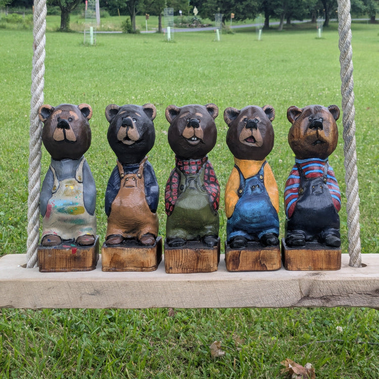 Hand crafted wood carved bear figurines in different outfits on a swing set with a grassy background